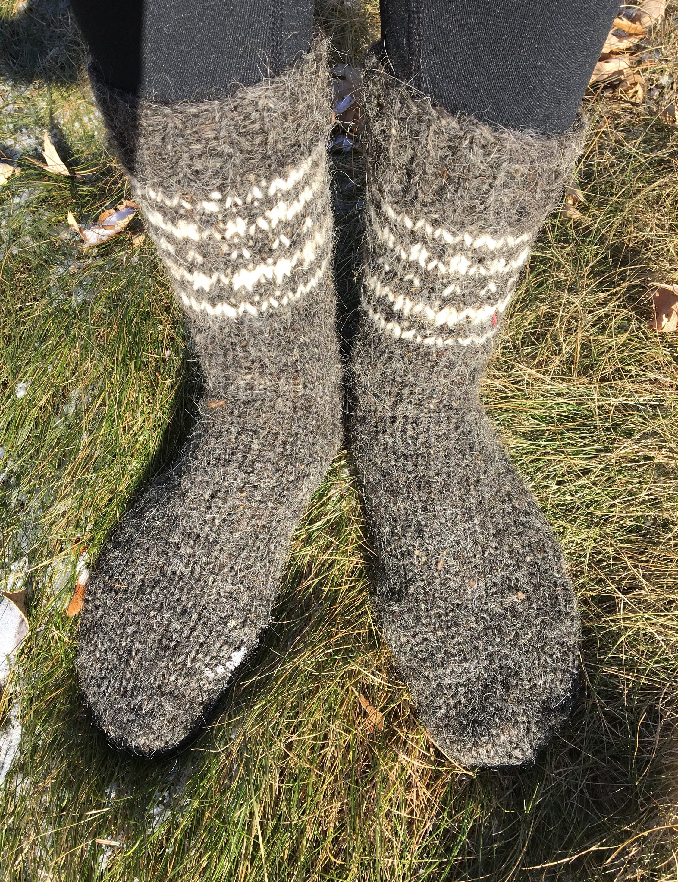 Hand-knitted wool socks made from pure sheep wool, unisex winter wear displayed outdoors on grass.