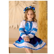 Girl in traditional Ukrainian Hutsul folk costume with blue woven blouse and skirt, wearing a floral headband, sitting on a bench.