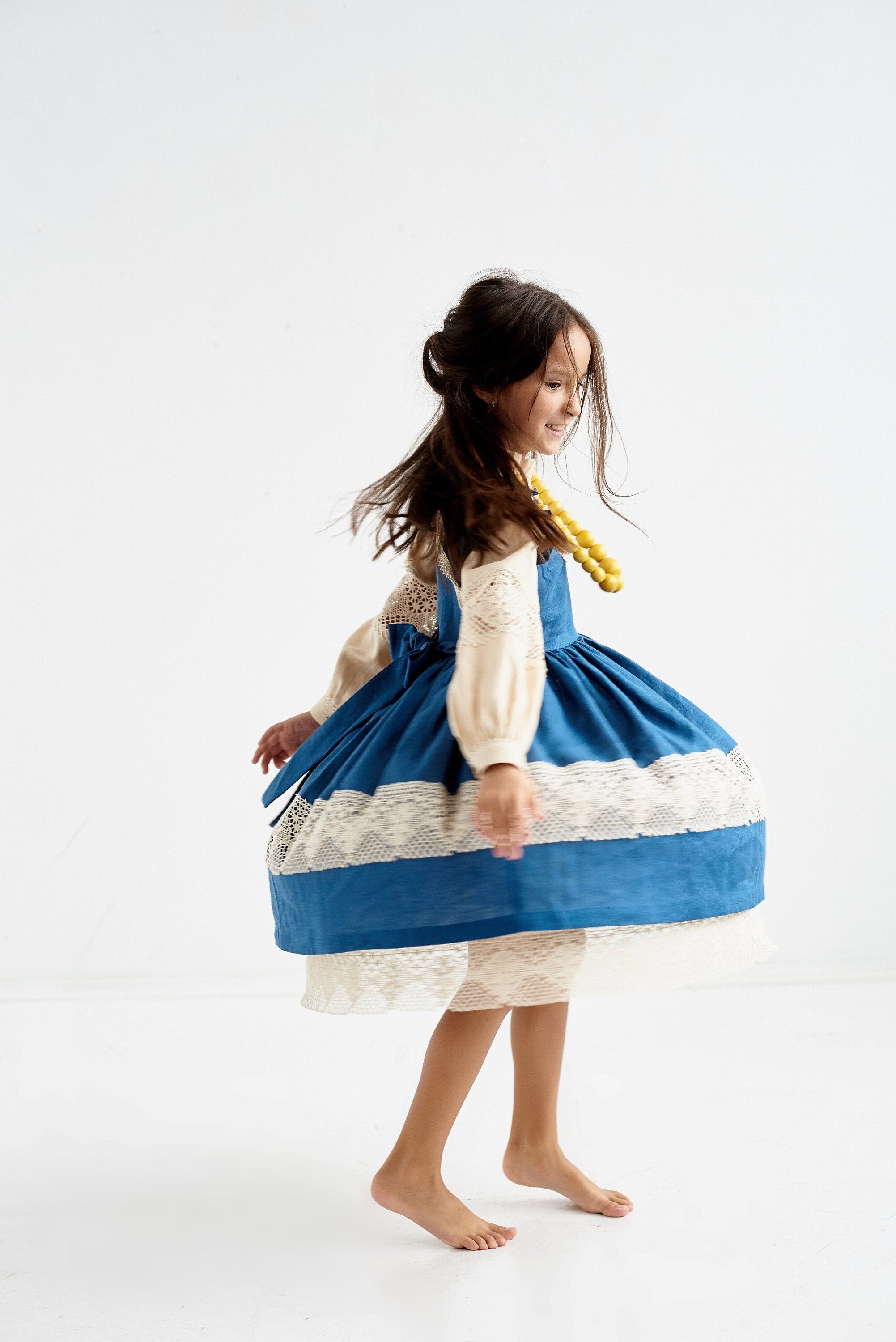 Child wearing a blue Ukrainian linen dress with lace trim and puff sleeves, spinning around playfully.