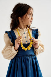 Young girl wearing a blue Ukrainian linen dress with puff sleeves, lace trim, and yellow bead necklace, in a traditional boho style.