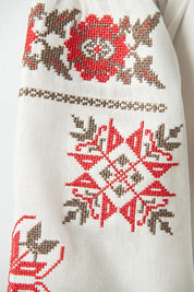 Embroidered sleeve detail of Ukrainian linen girls' shirt with red floral ornament.