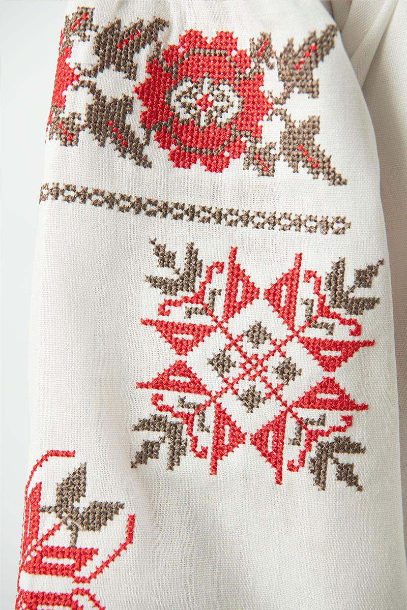 Embroidered sleeve detail of Ukrainian linen girls' shirt with red floral ornament.