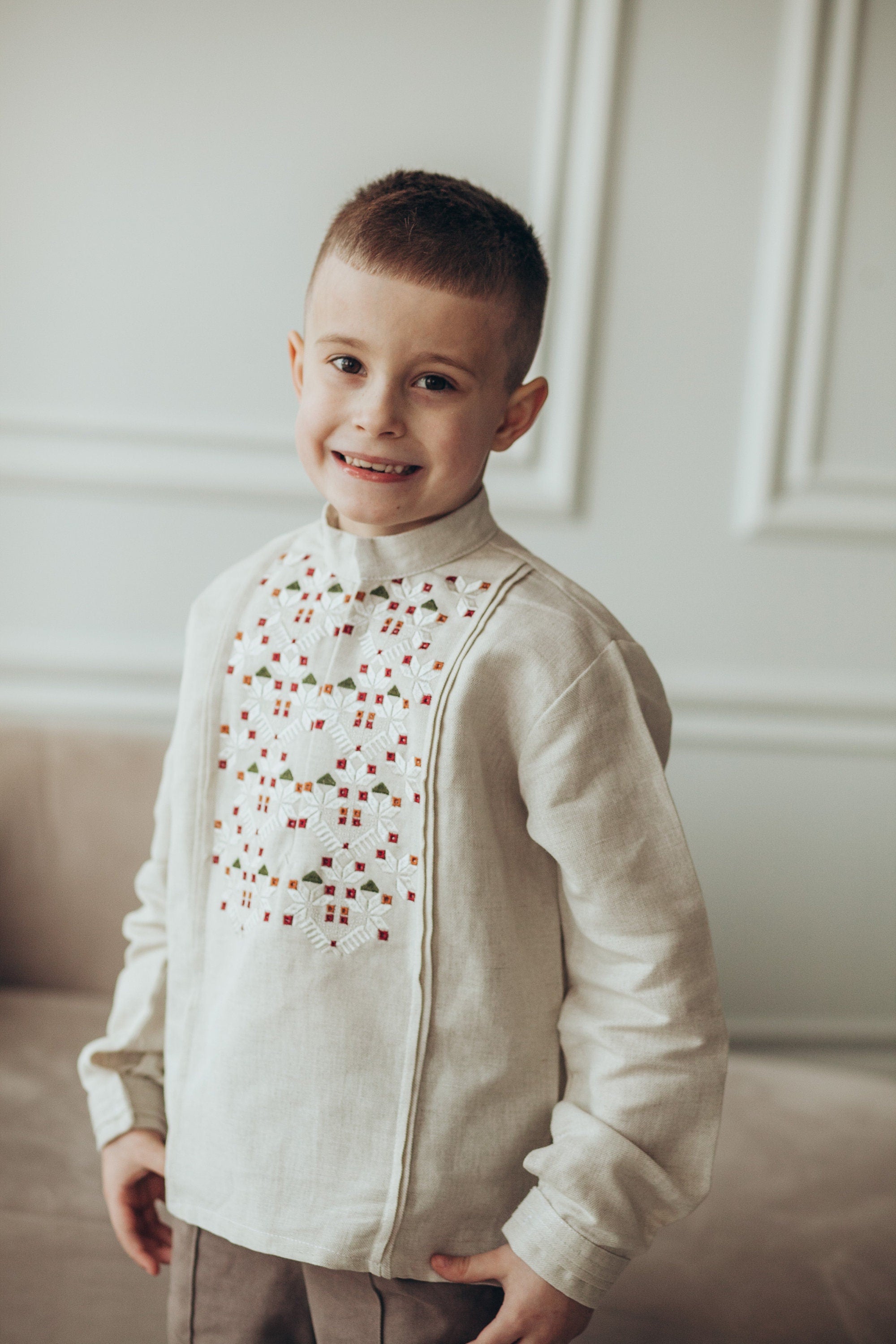 Smiling young boy wearing a traditional Ukrainian embroidered vyshyvanka shirt in white linen with long sleeves.