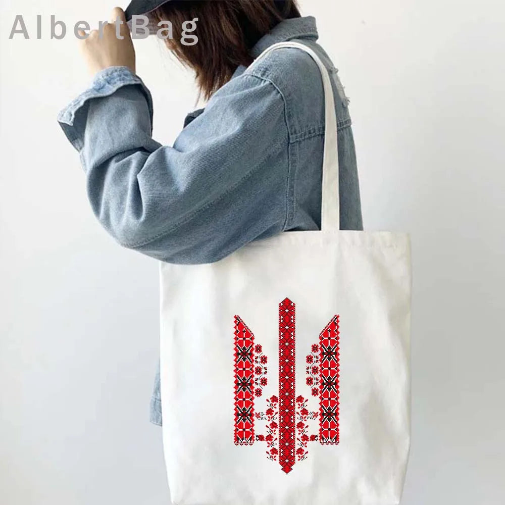 Woman carrying Ukrainian patriotic grocery tote bag with traditional red pattern.