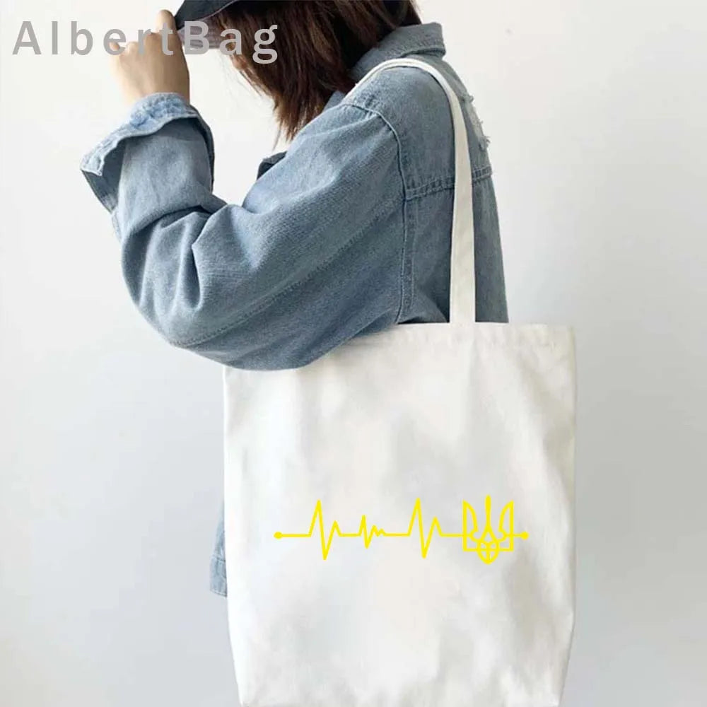 Ukrainian Patriotic Grocery Tote Bag with yellow heartbeat design carried by woman in denim shirt. Eco-friendly and reusable.