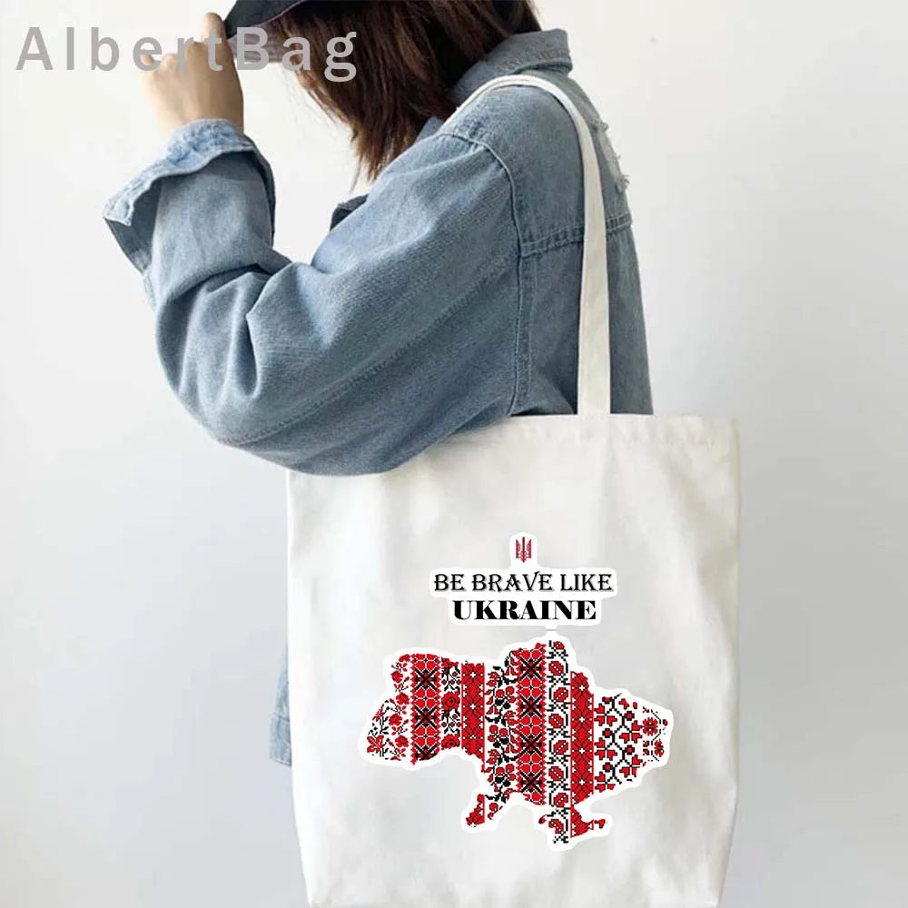 Woman carrying Ukrainian Patriotic Grocery Tote Bag with "Be Brave Like Ukraine" print and red embroidered map design.