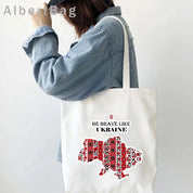 Woman carrying Ukrainian Patriotic Grocery Tote Bag with "Be Brave Like Ukraine" print and red embroidered map design.