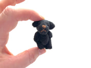 Hand holds a tiny black fuzzy teddy bear with moveable arms and legs, suitable for hanging decoration or keychain accessory.