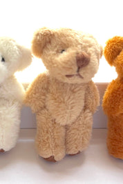 Three tiny soft, fuzzy hand-sewn teddy bears in cream, light brown, and orange, standing in a row, perfect for decoration.