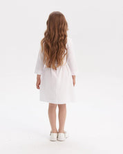 Child wearing white Ukrainian embroidered dress, back view with long brown hair, showcasing traditional vyshyvanka style.