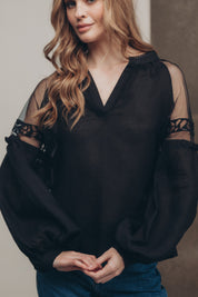 Black-on-black embroidered Ukrainian blouse with tulle shoulder inserts in boho ethnic style, worn by woman with loose waves.