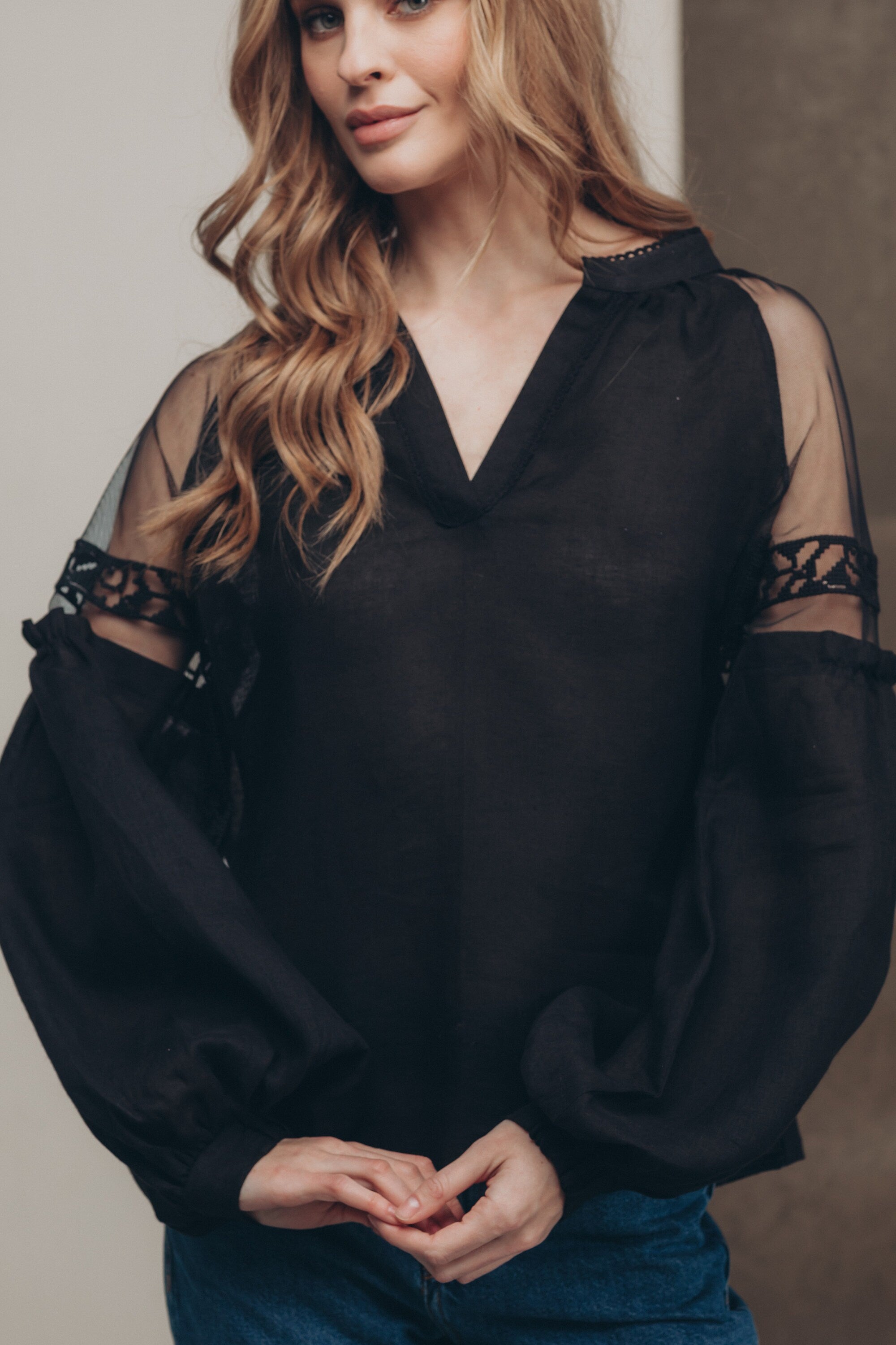 Black-on-black embroidered Ukrainian blouse with tulle shoulder inserts in boho ethnic style, worn by woman with loose waves.