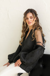 Woman wearing black-on-black Ukrainian embroidered blouse with tulle shoulder inserts, highlighting elegant boho ethnic style.