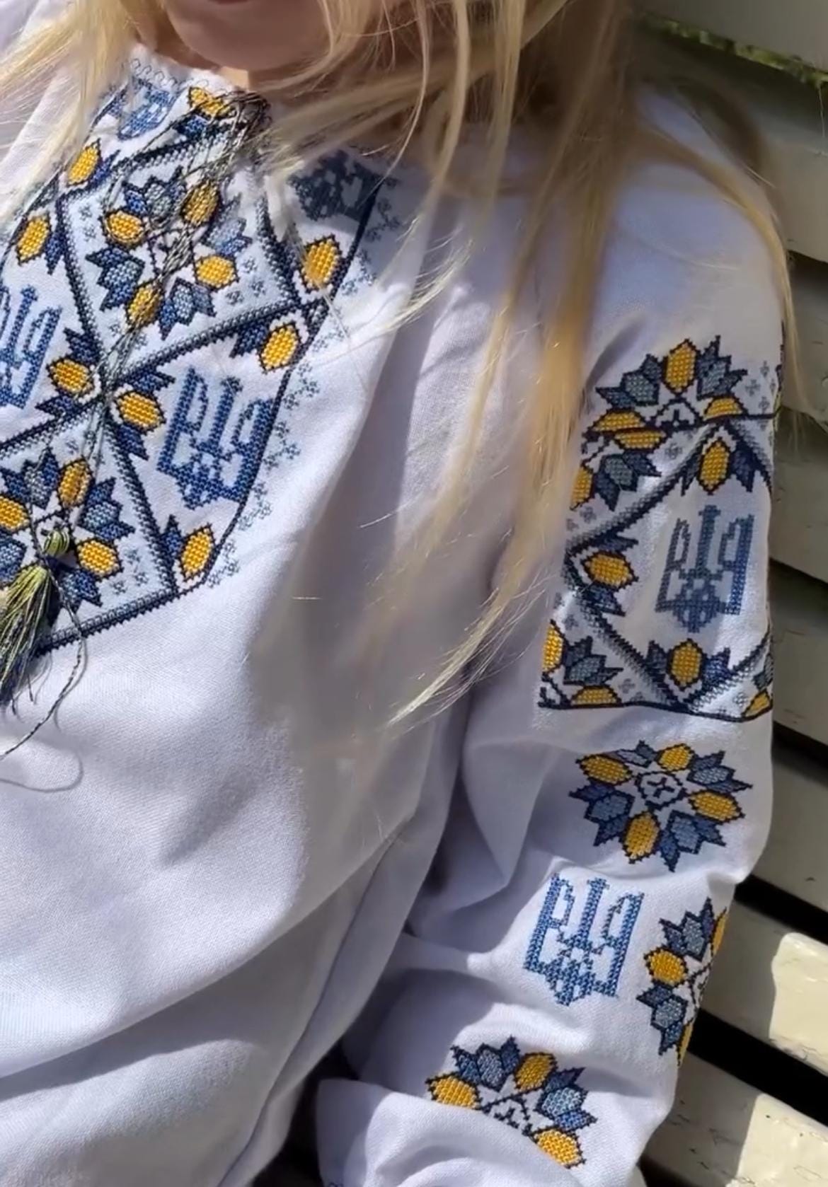 Close-up of girl's embroidered Ukrainian vyshyvanka dress with Tryzub symbol in blue and yellow cross-stitch design.