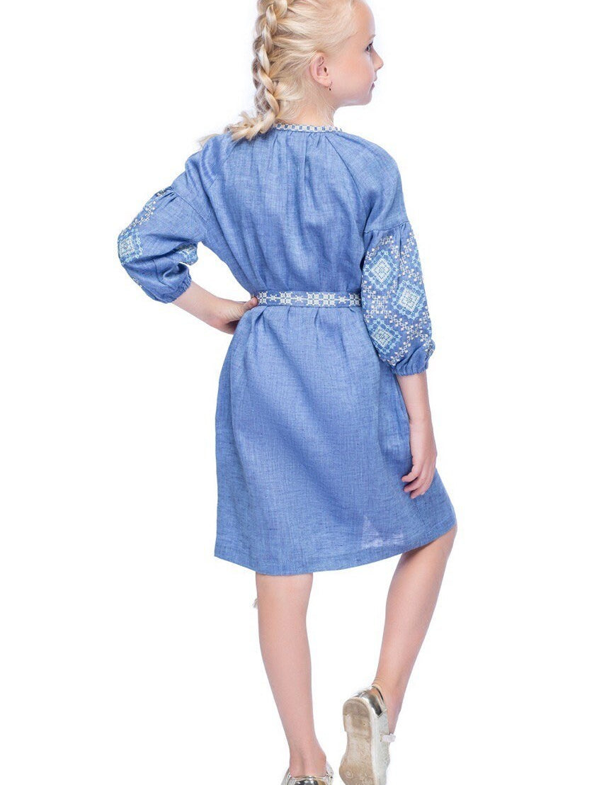 Girl wearing blue embroidered linen dress with traditional Ukrainian patterns and floral cross-stitch, side view.