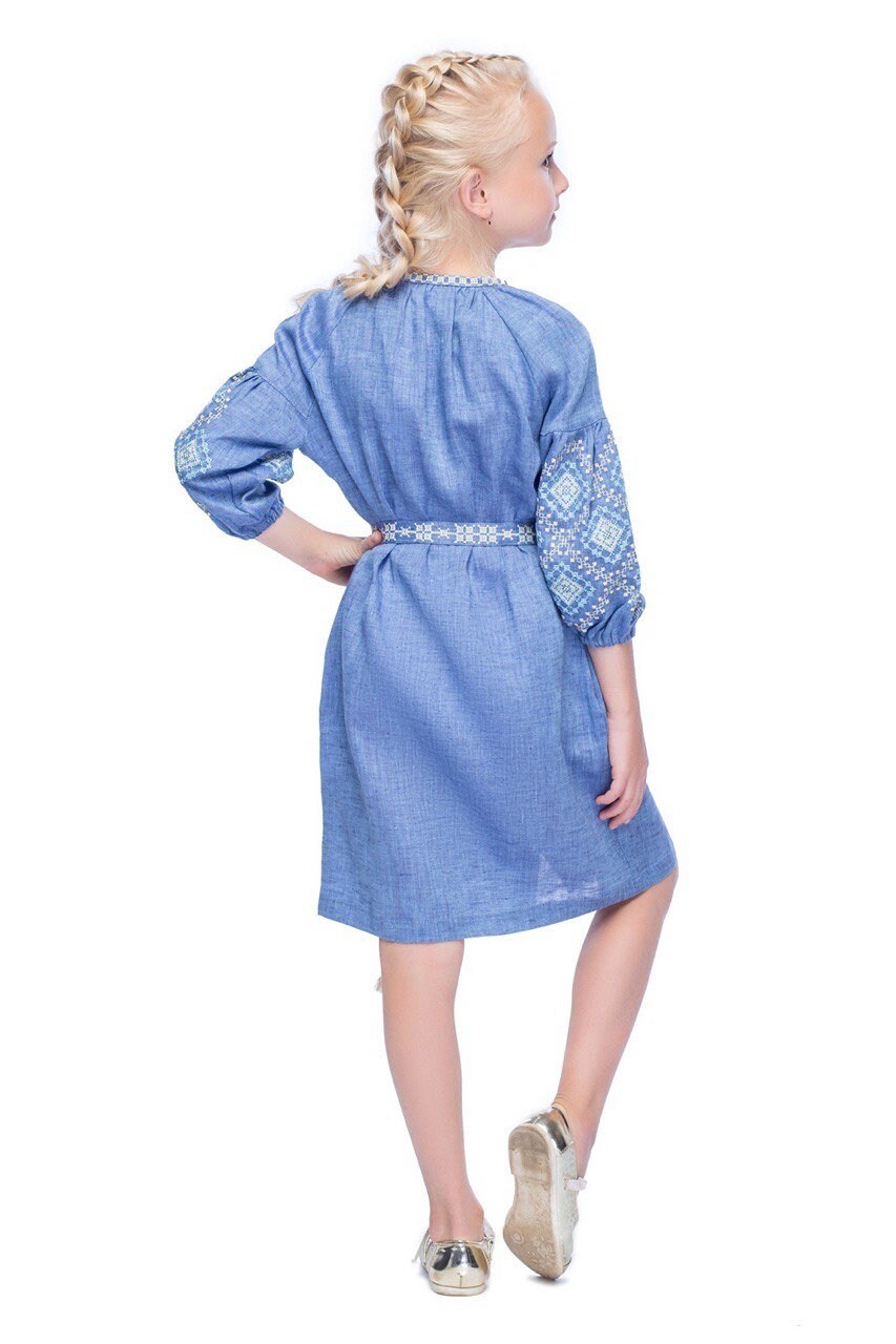 Girl wearing blue embroidered linen dress with traditional Ukrainian patterns and floral cross-stitch, side view.