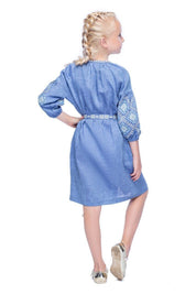 Girl wearing blue embroidered linen dress with traditional Ukrainian patterns and floral cross-stitch, side view.