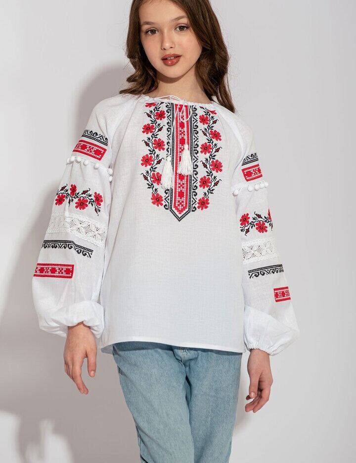 Child wearing Ukrainian white vyshyvanka shirt with red embroidery, showcasing folk design.