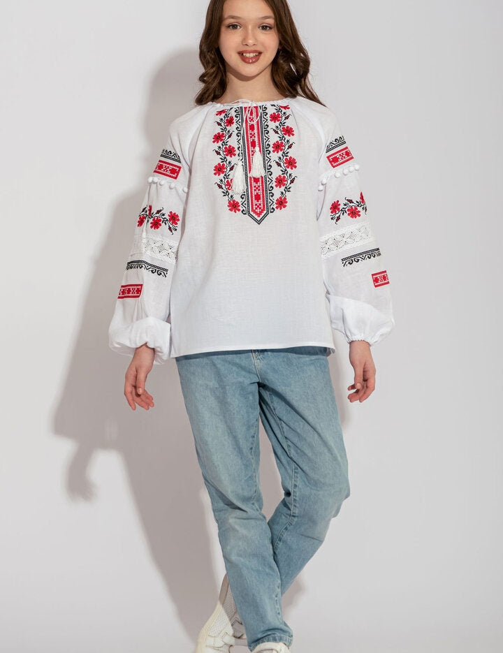 Child wearing Ukrainian white embroidered vyshyvanka shirt, featuring traditional red and black folk patterns, paired with blue jeans.
