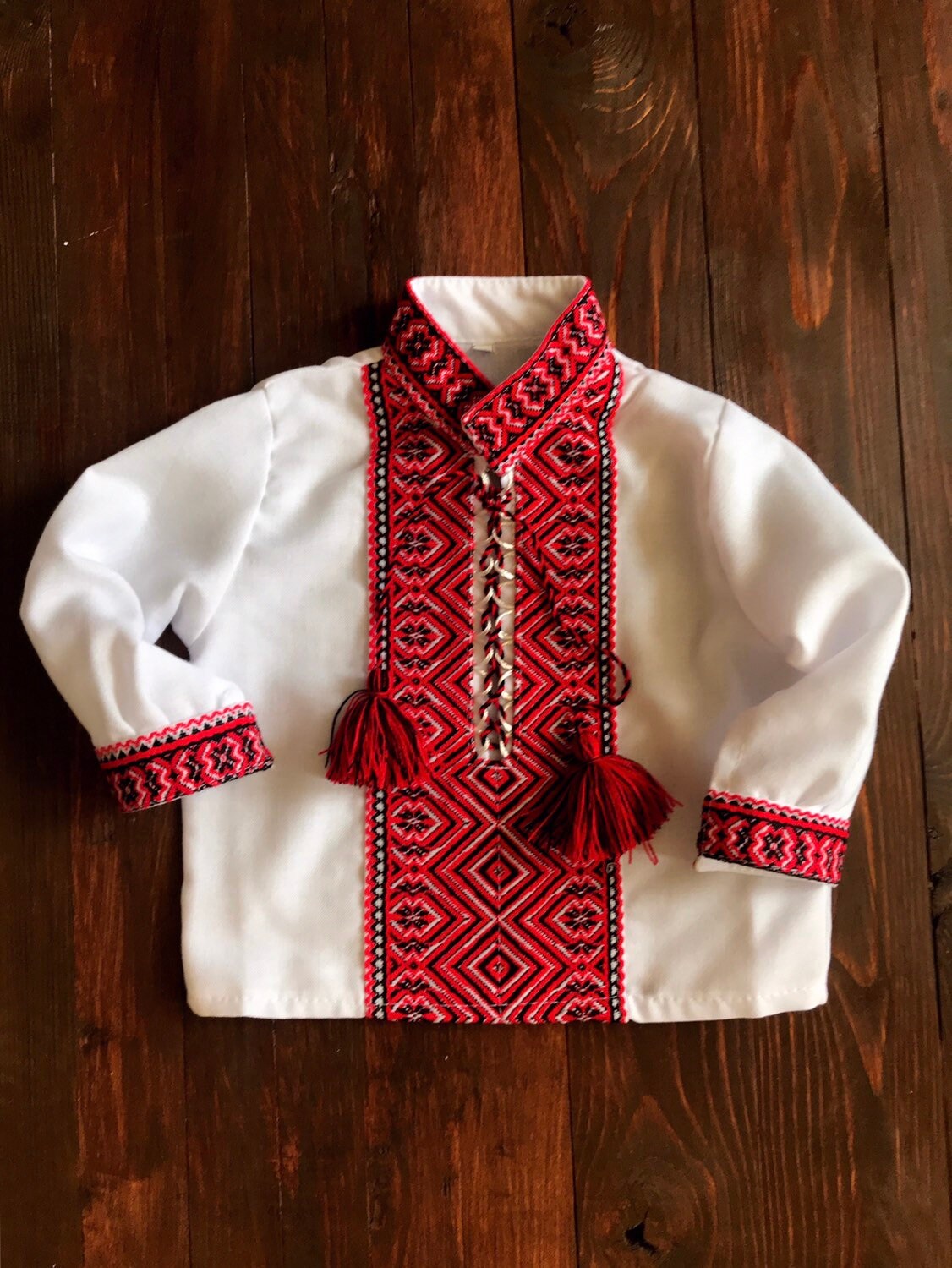 Traditional Ukrainian embroidered baby bodysuit with red and black patterns on white fabric, perfect for cultural events.