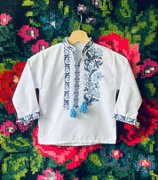 Embroidered Ukrainian boy's vyshyvanka shirt with blue traditional cross-stitch design on a floral background.