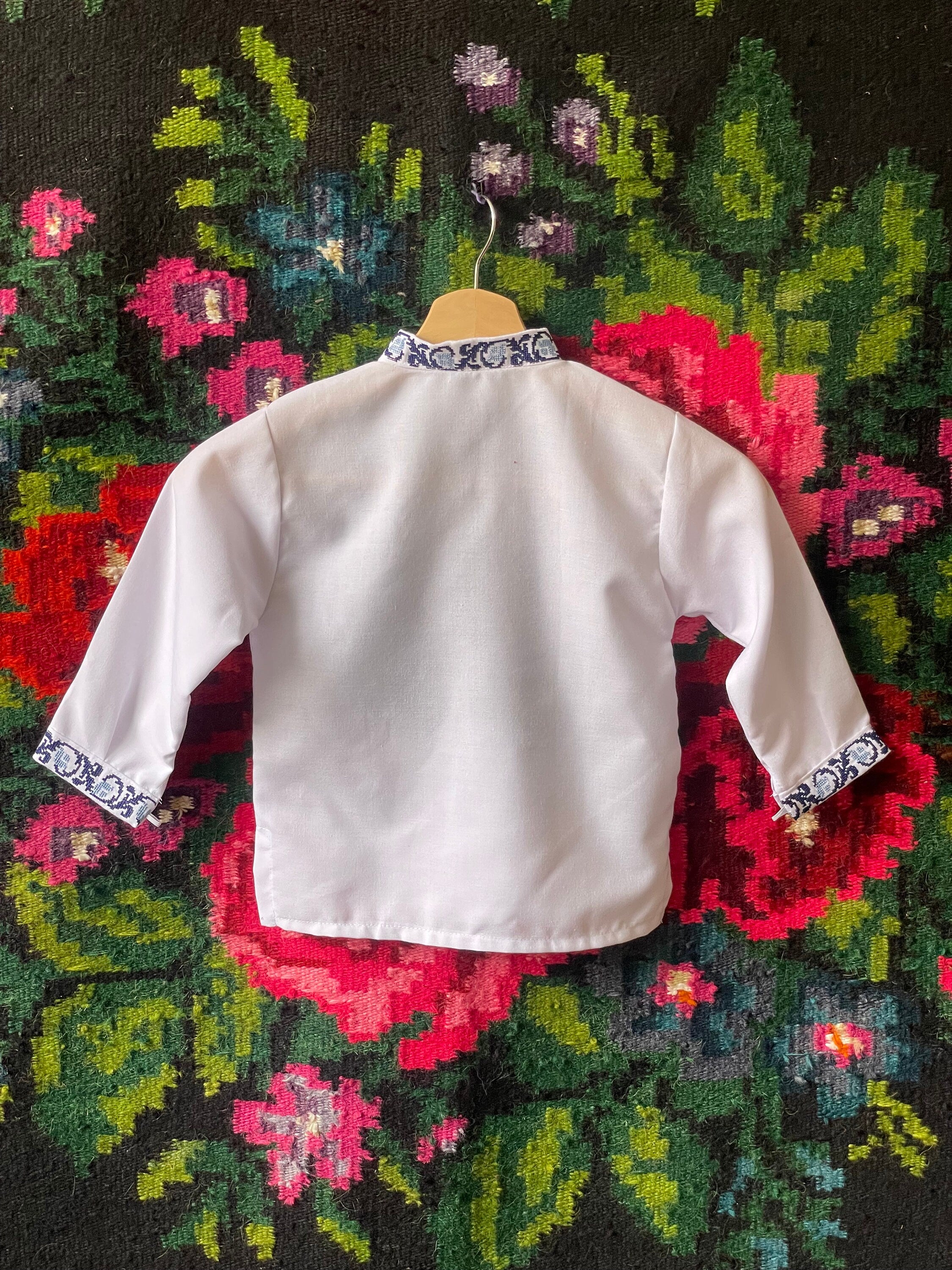 Ukrainian boy's vyshyvanka shirt with embroidered cuffs and collar, displayed on floral background.