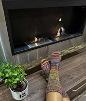 Colorful hand knitted wool socks by a cozy fireplace with a potted plant