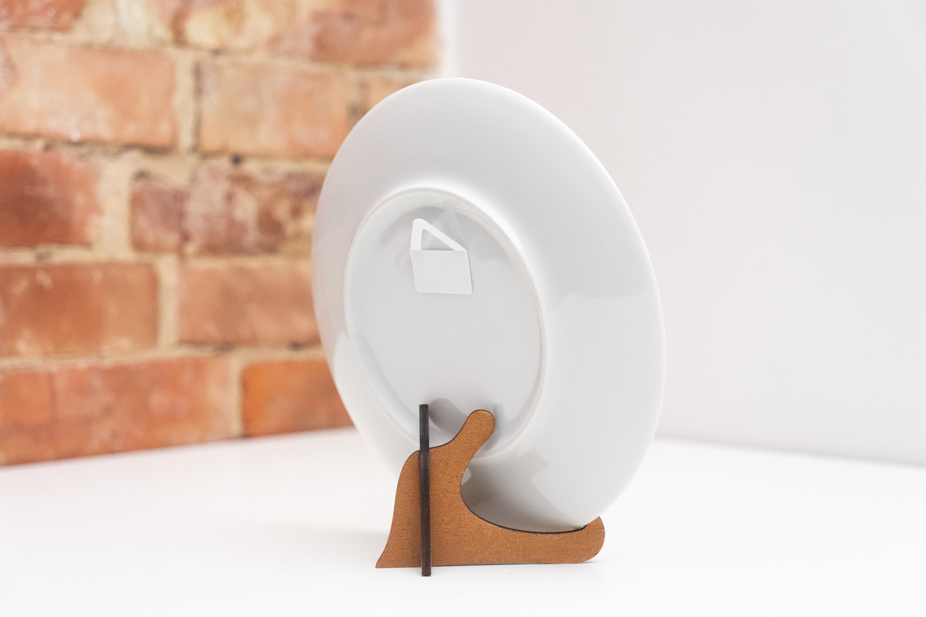 Back view of a porcelain wall plate on a wooden stand against a brick wall backdrop.