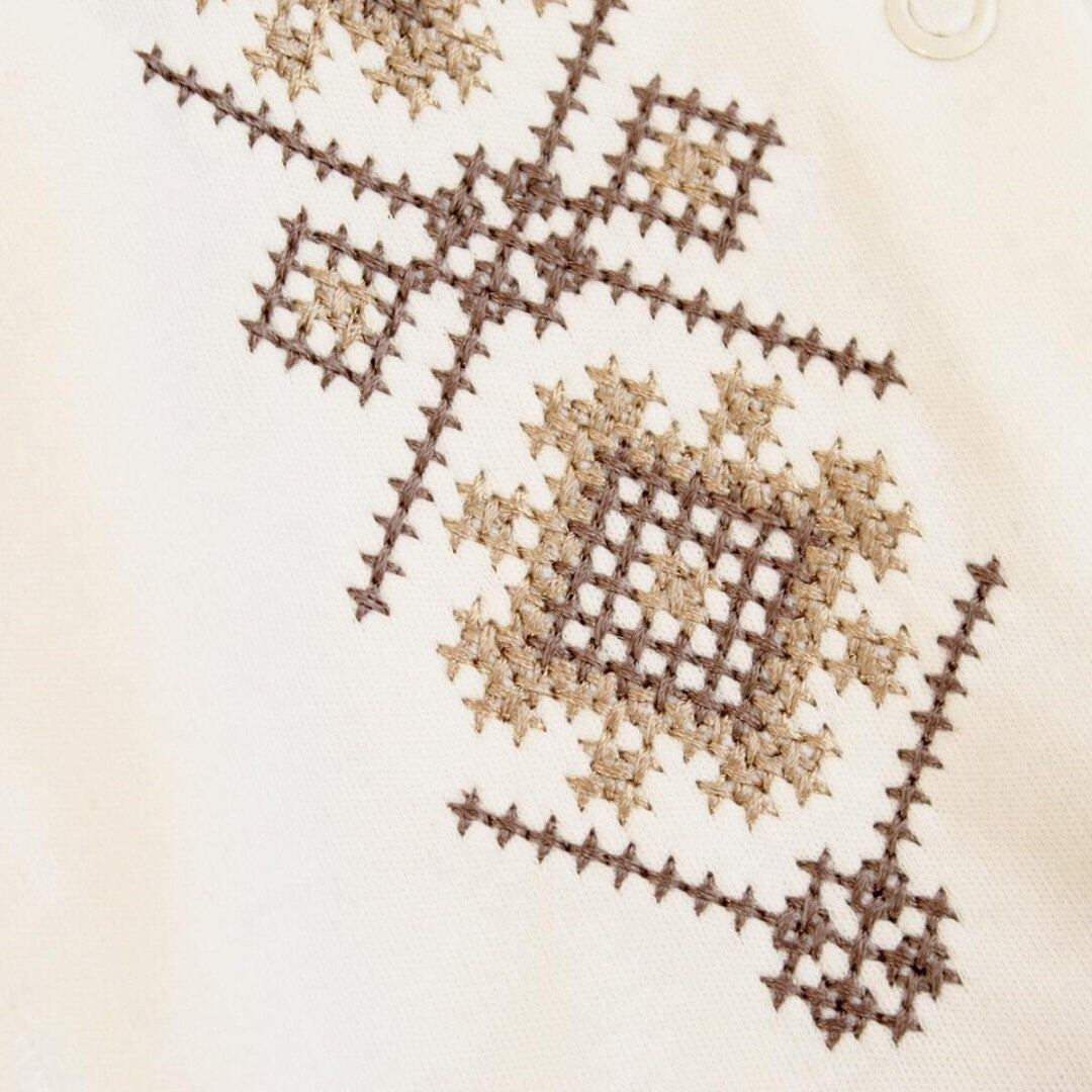 Traditional Ukrainian embroidery in beige and brown on a baby romper, showcasing detailed Vyshyvanka patterns.