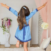 Girl wearing traditional Ukrainian embroidered dress, blue, with arms raised in room with floral decor and plush seating.