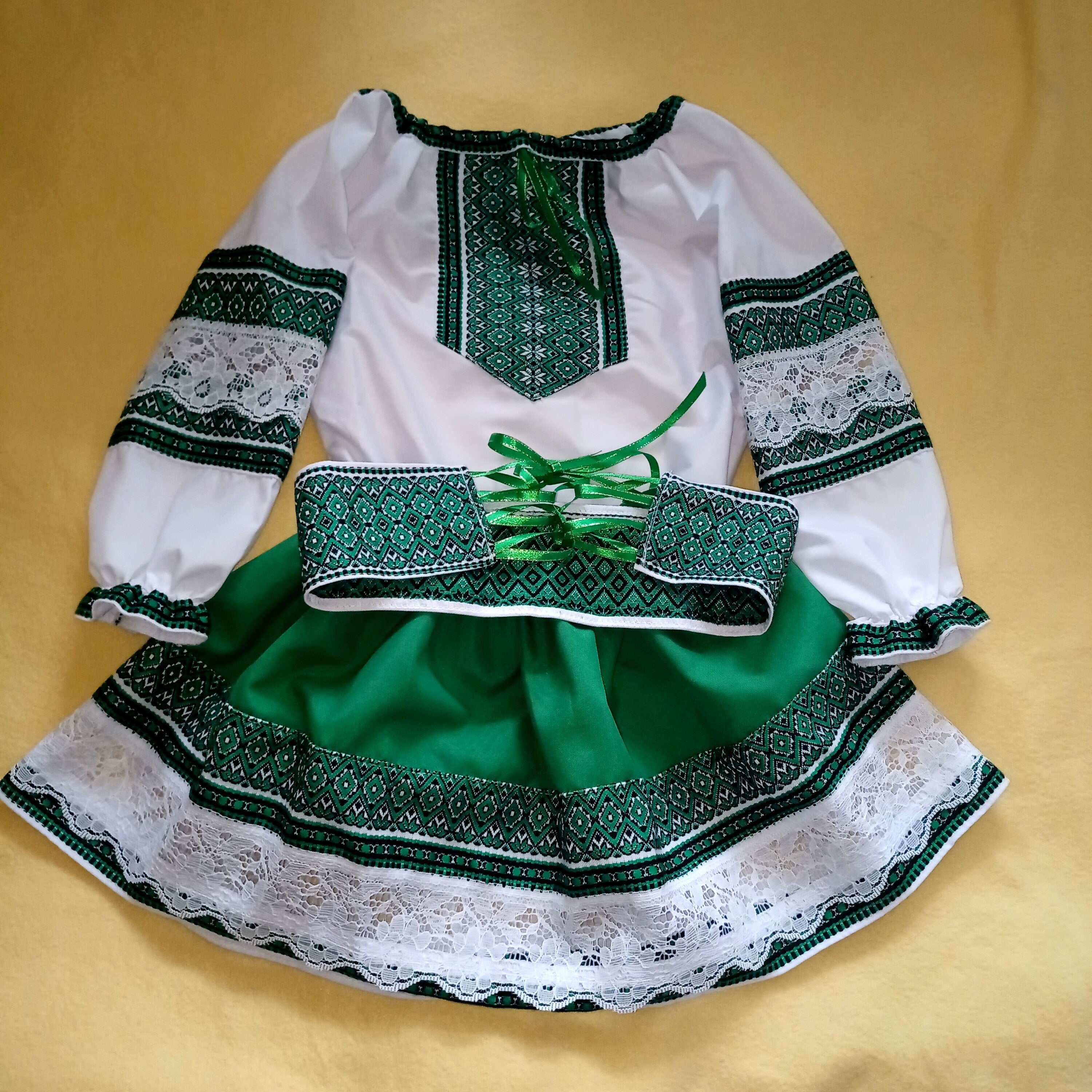 Girl's green and white embroidered Ukrainian blouse and skirt set featuring traditional patterns on a yellow background.