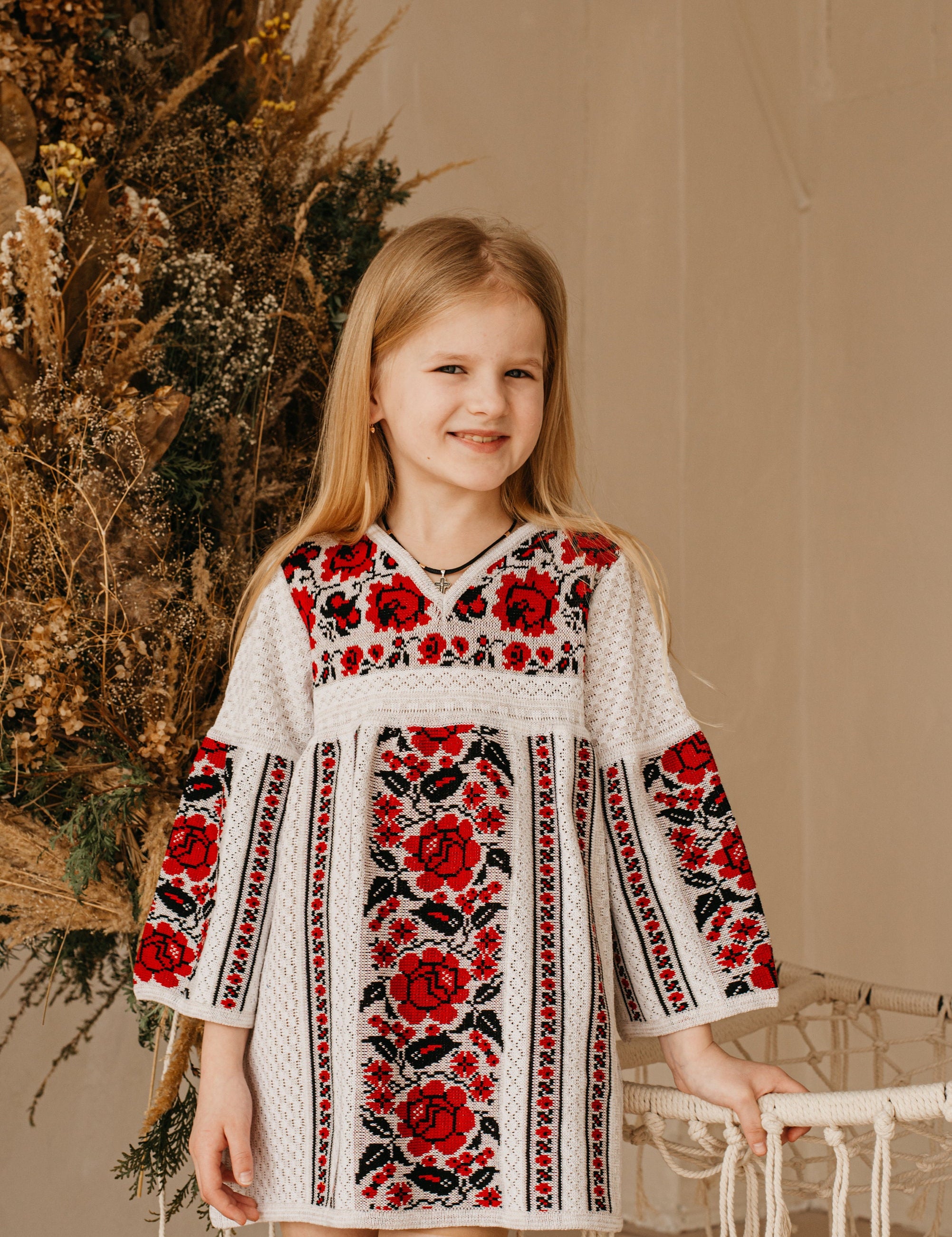 Girl in Ukrainian embroidered knit dress with red floral design, traditional Vyshyvanka style, cotton clothing for children.