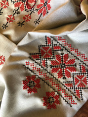 Close-up of Ukrainian Vyshyvanka embroidery with red floral Rosava motif on linen fabric for traditional dresses.