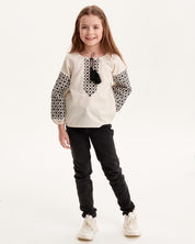 Girl wearing Ukrainian embroidered vyshyvanka shirt with Slavic folk art design, paired with black pants.