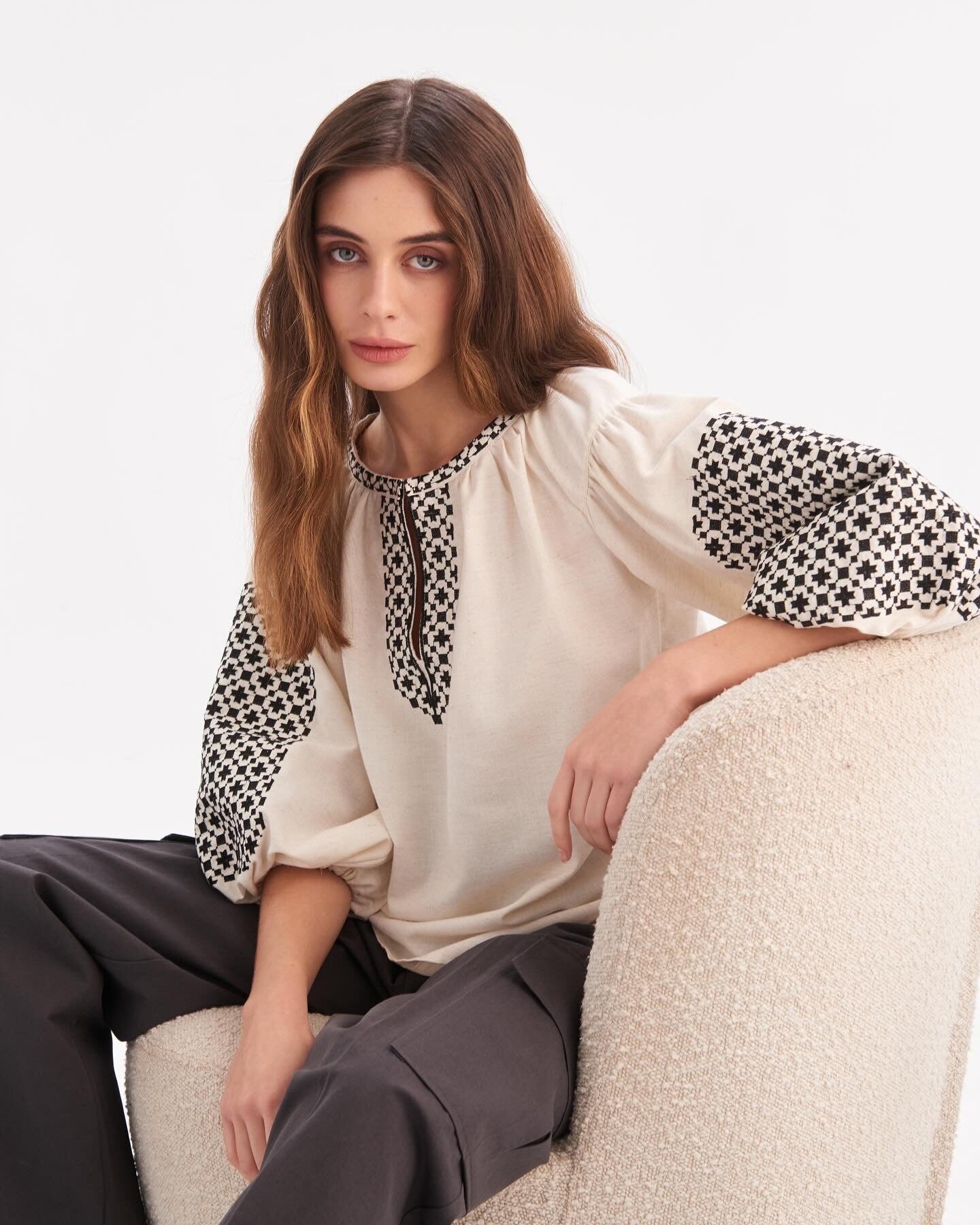 Woman wearing Ukrainian embroidered shirt with Slavic folk art motifs, seated on a chair.