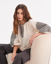 Woman wearing Ukrainian embroidered shirt with Slavic folk art motifs, seated on a chair.