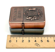 Ukrainian gasoline lighter with bronze and silver coat of arms next to a ruler, showcasing intricate national symbol design.