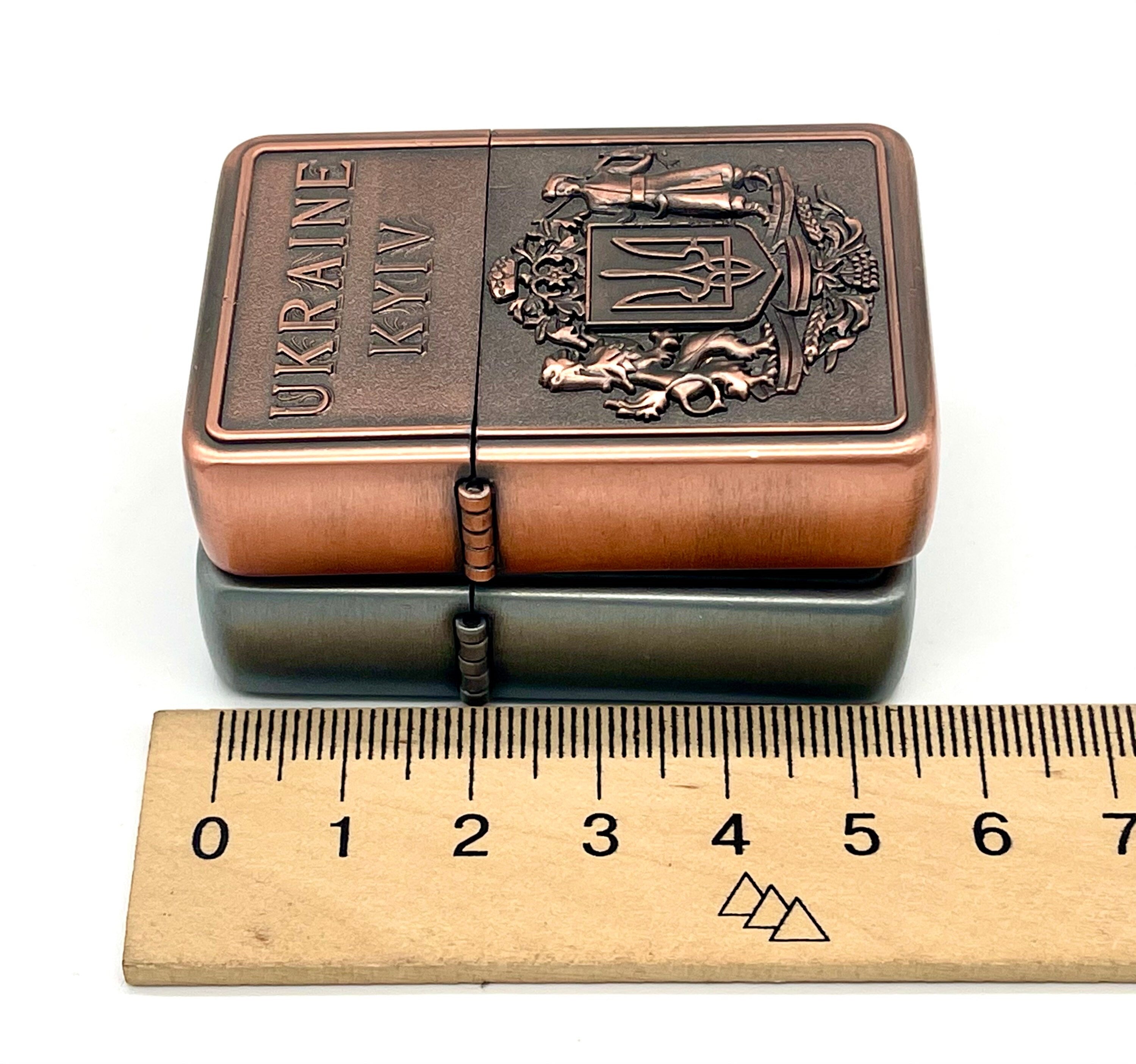 Ukrainian gasoline lighter with bronze and silver coat of arms next to a ruler, showcasing intricate national symbol design.