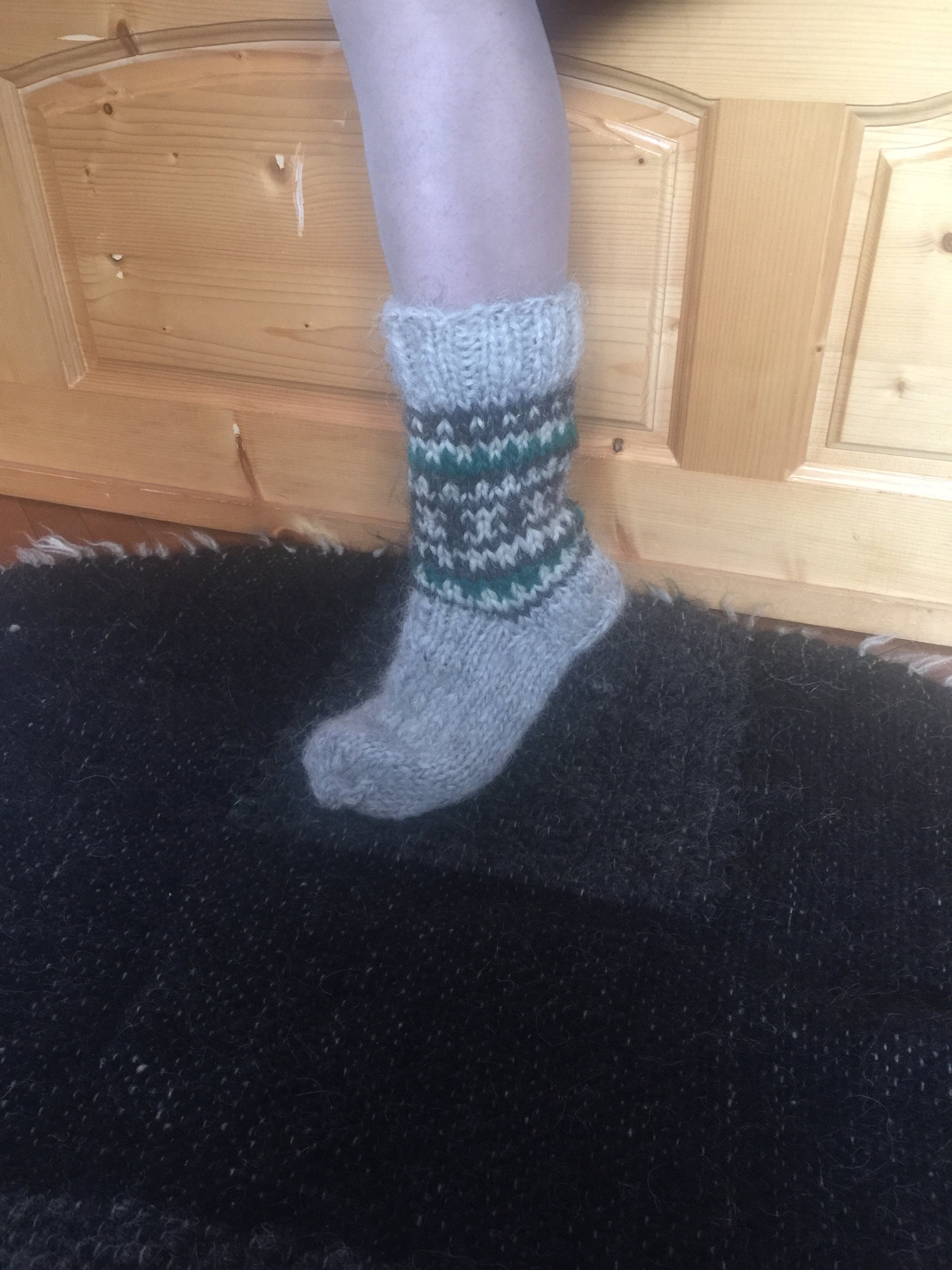 Hand-knitted wool sock from Ukraine with green and gray pattern, resting on black rug.