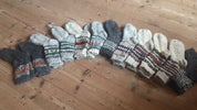 Array of handmade wool socks with colorful patterns laid on wooden floor.