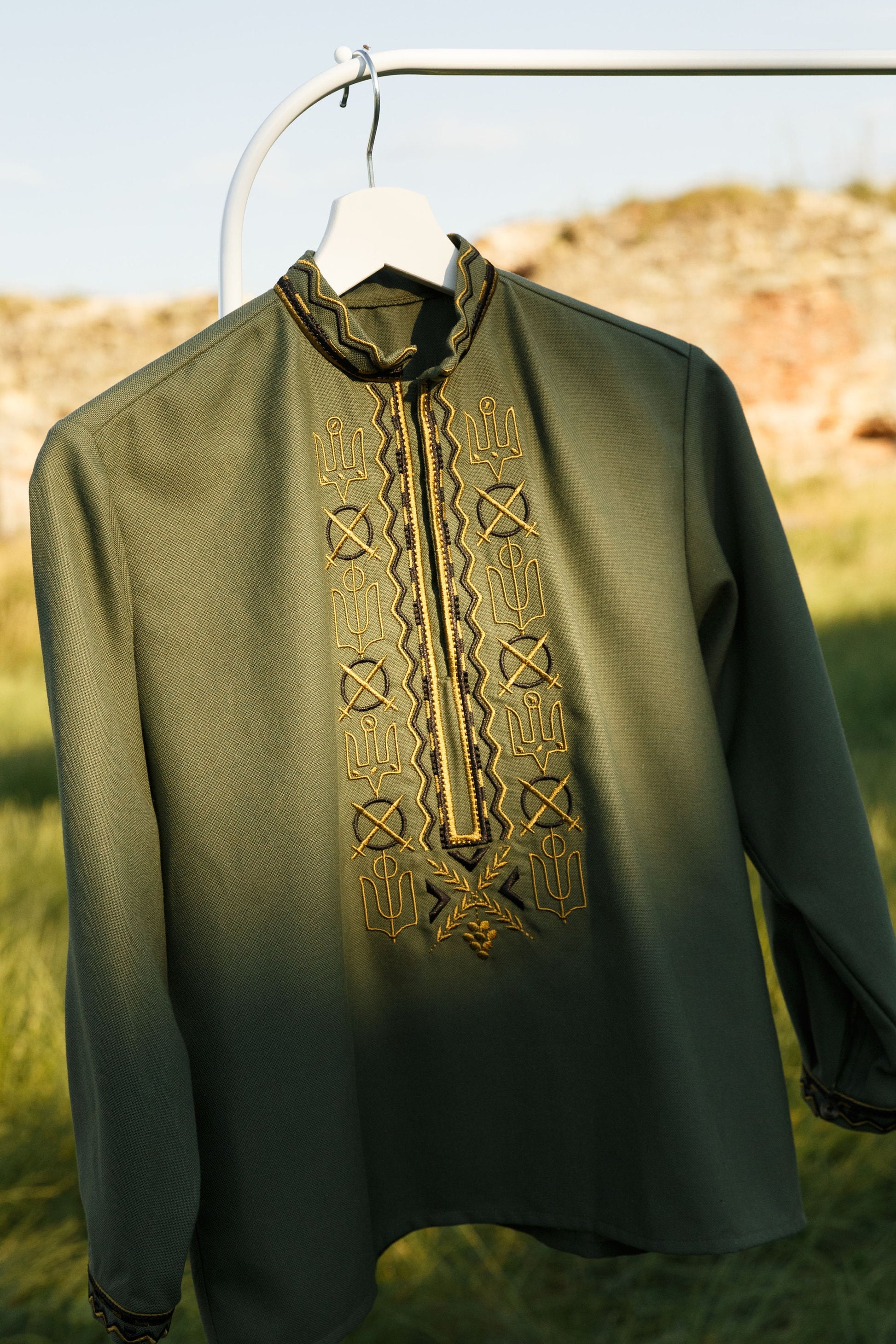 Ukrainian embroidered military-style Vyshyvanka shirt for men, inspired by Zelensky, hanging outdoors on a hanger.