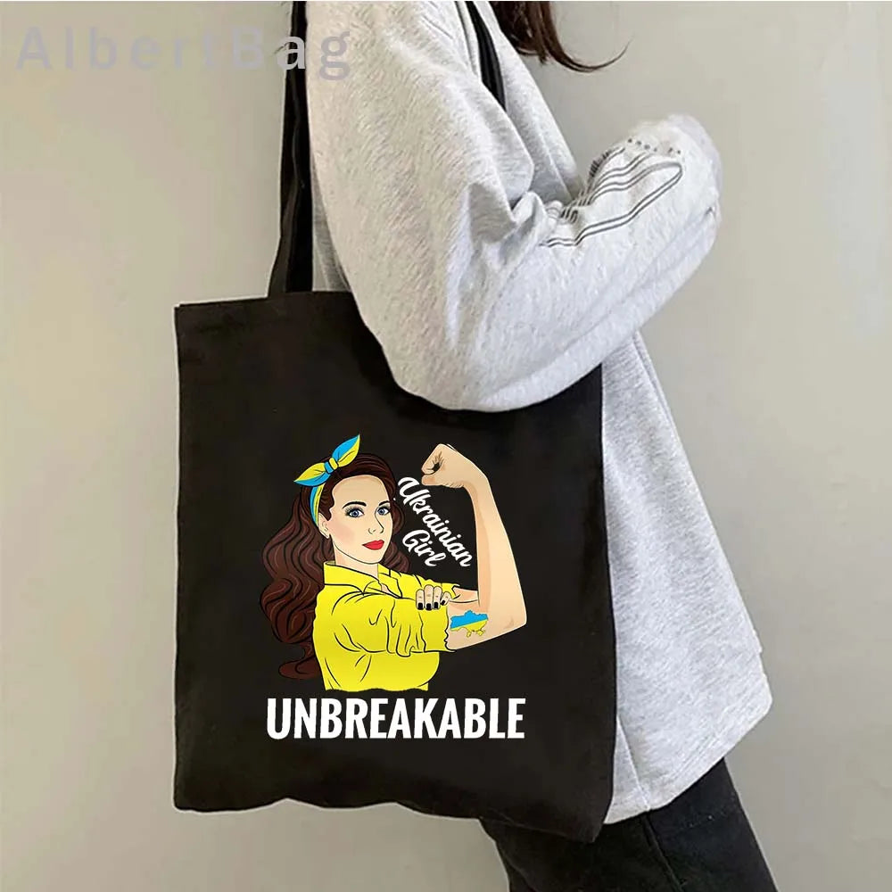Black tote bag with "Ukrainian Girl Unbreakable" design, featuring a strong woman graphic in yellow on a cotton fabric.