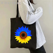Black Ukrainian patriotic tote bag with blue and yellow sunflower design carried by a person in a gray sweater.