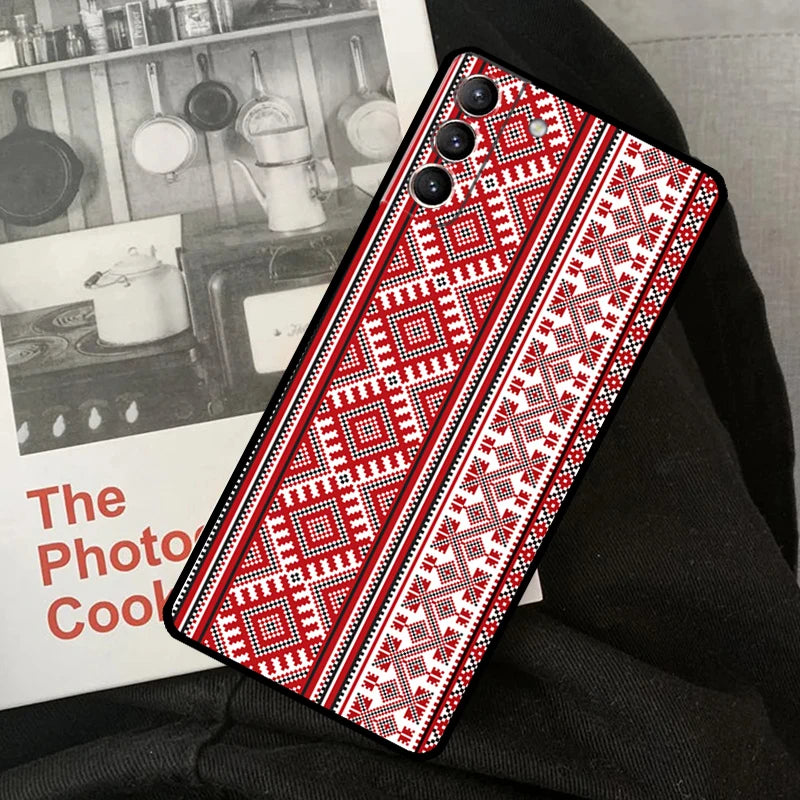 Ukrainian pattern phone case for Samsung Galaxy, featuring red and black intricate ornaments, shown on knees next to a photo book.
