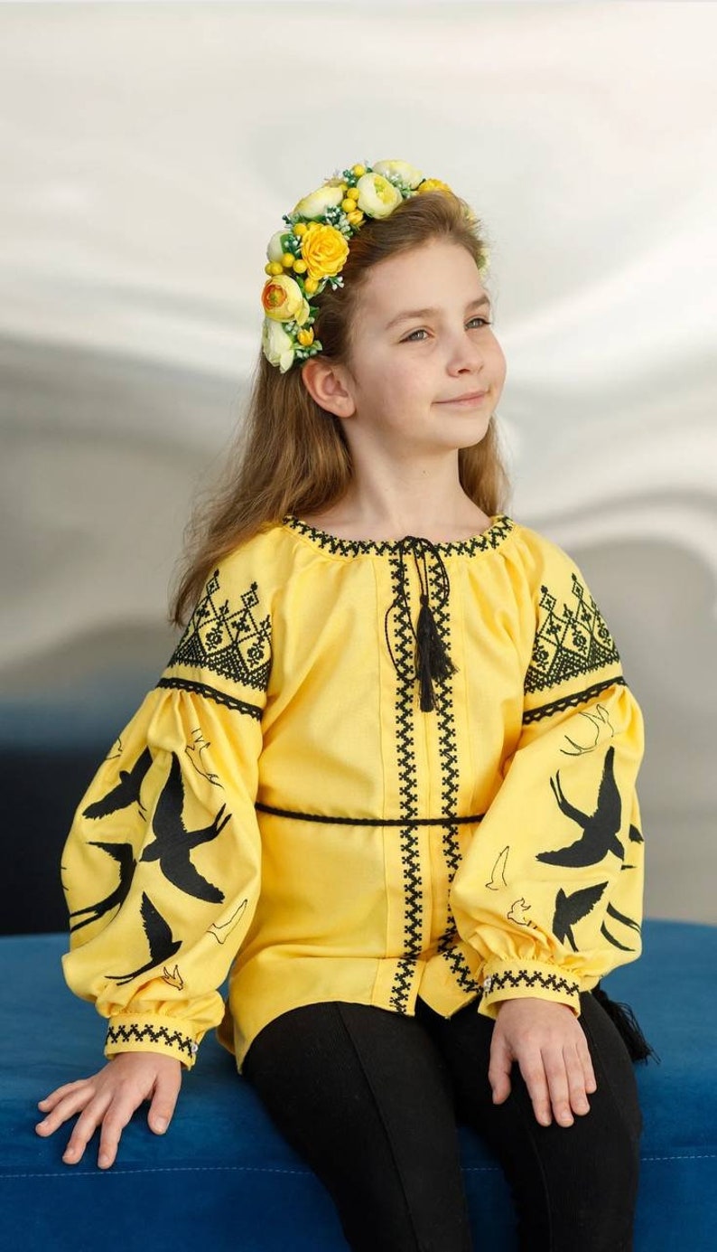 Girl wearing Ukrainian blouse with blue and yellow swallow embroidery, ideal for festive occasions.