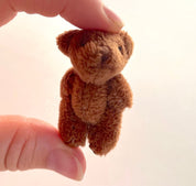 Hand holding a tiny soft fuzzy stuffed teddy bear with movable arms and legs, perfect for decoration or as a cute companion.