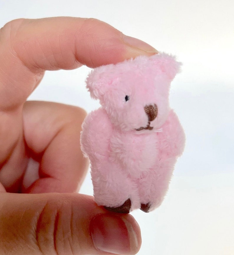 Hand holding tiny soft pink fuzzy teddy bear with moveable arms and legs, perfect for decoration or keychain accessory.