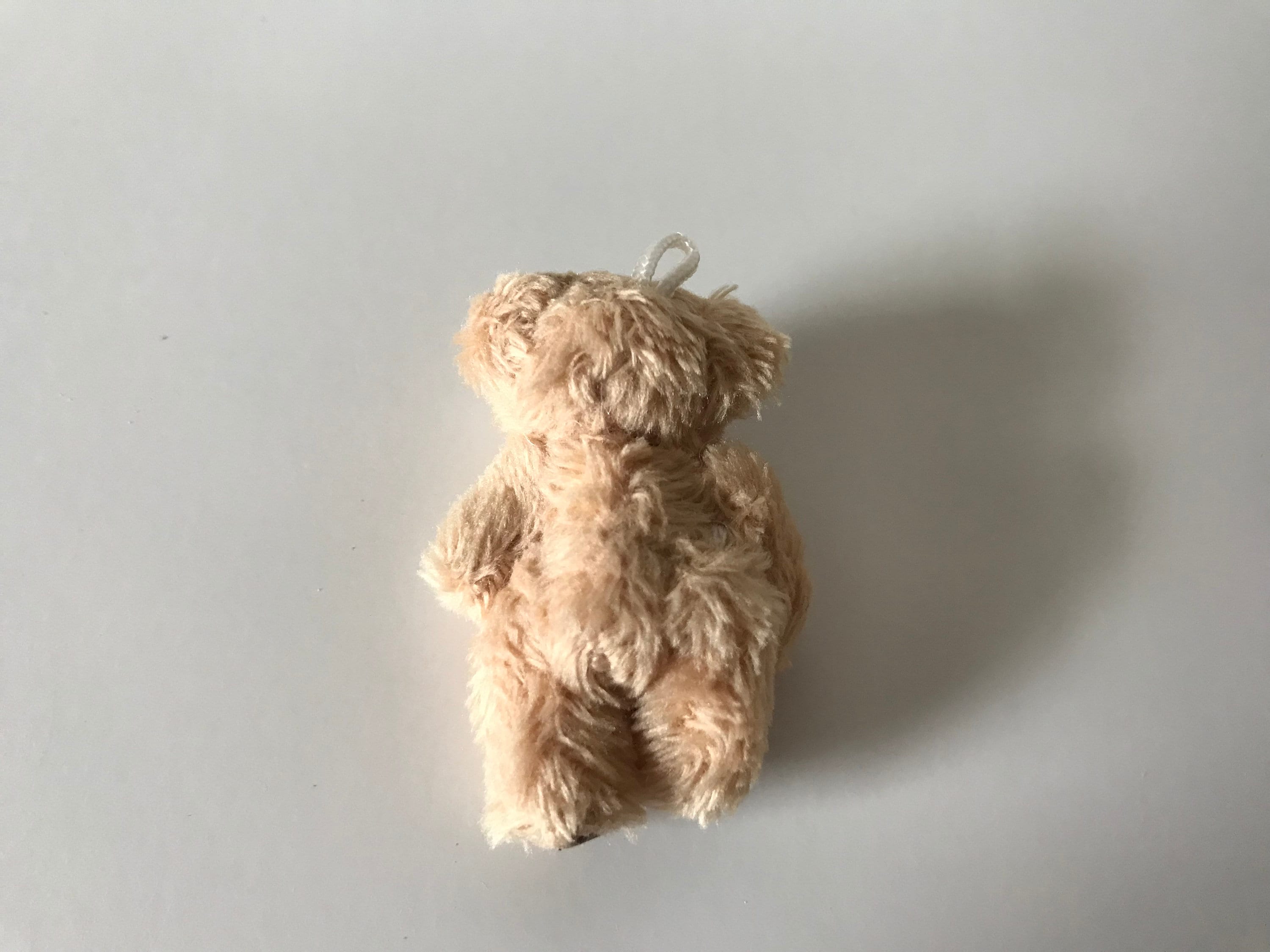 Miniature hand-sewn fuzzy teddy bear with moveable limbs and hanging loop, designed for decoration and play, suitable for ages 6+.