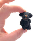Hand holding a tiny soft black fuzzy stuffed teddy bear with moveable arms and legs, perfect for decoration or a child’s small companion.