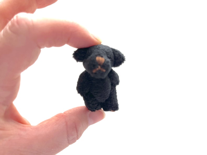 Hand holding a tiny soft black fuzzy stuffed teddy bear with moveable arms and legs, perfect for decoration or a child’s small companion.